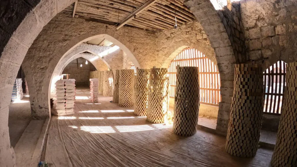 High cylindrical towers of stacked Aleppo soap blocks drying under stone arches in a traditional Syrian workshop.