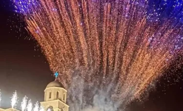 A night photograph of Our Lady of Saidnaya Monastery in Syria illuminated by a large display of blue and orange fireworks during a festival.