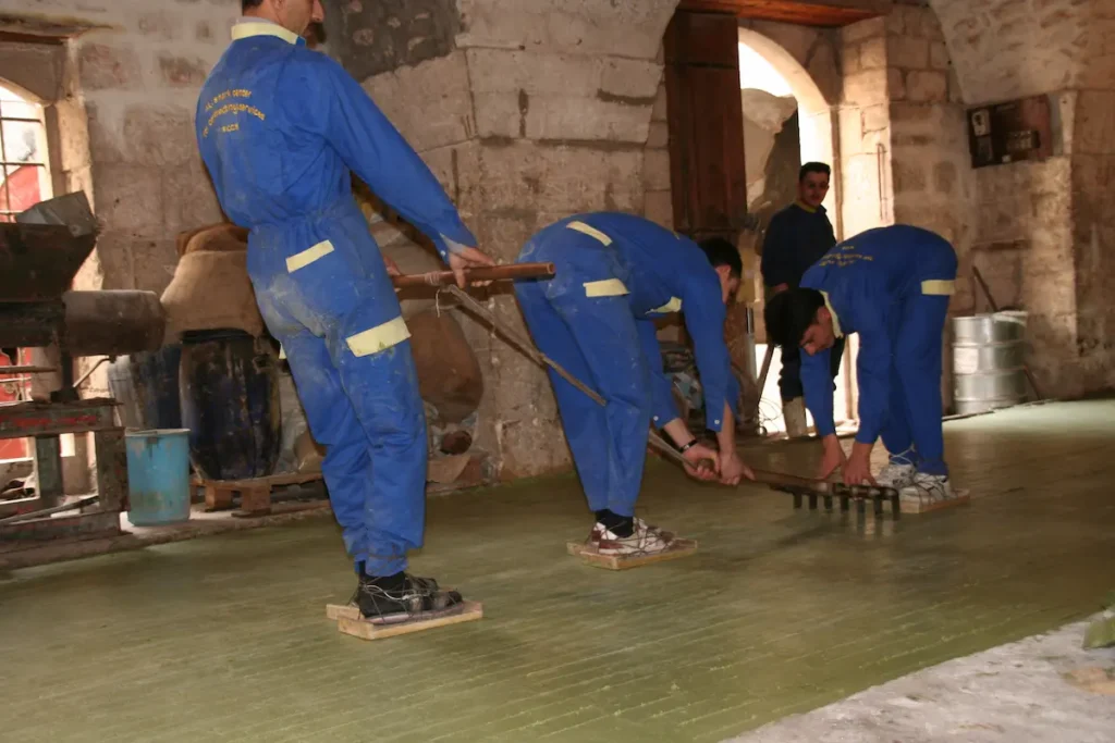 Skilled Syrian artisans in a historic Aleppo workshop using traditional manual tools to cut blocks of handmade laurel soap.