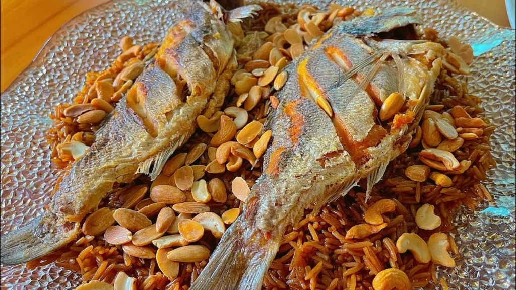 A close-up view of a large platter featuring two whole fried fish served over a generous mound of dark, caramelized onion-spiced rice, topped with a scattering of toasted almonds and cashews.